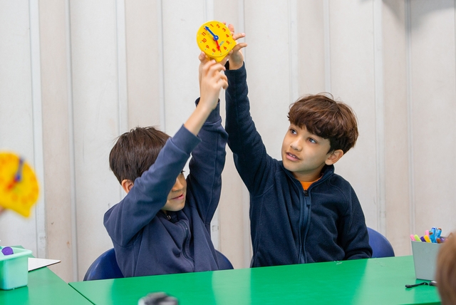 Two young boys holding up a clock together.