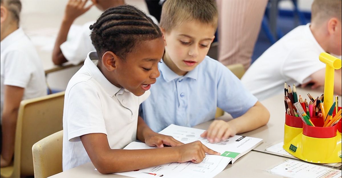 Two young boys looking at a Maths — No Problem! textbook together while engaging in discussion.