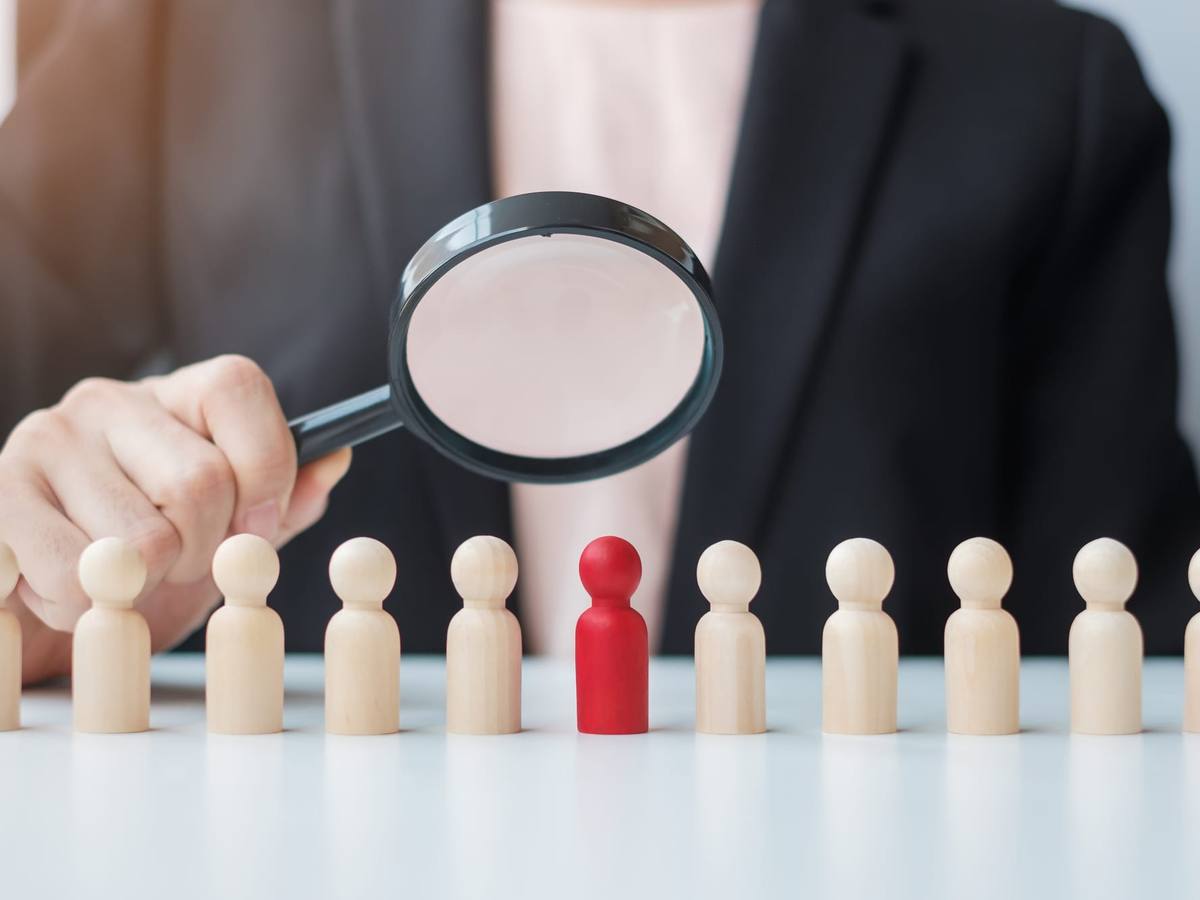 A magnifying glass held over a row of wooden figures, one picked out in red
