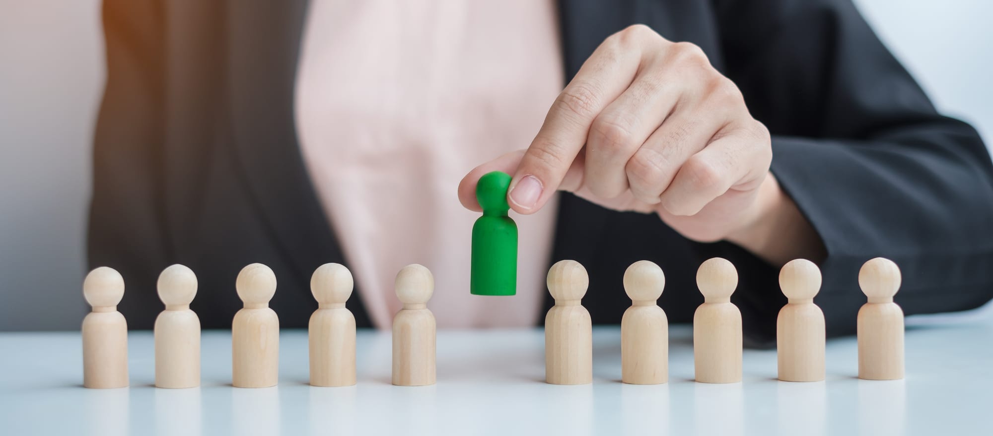 A hand lifting one green figure out of a row of wooden figures