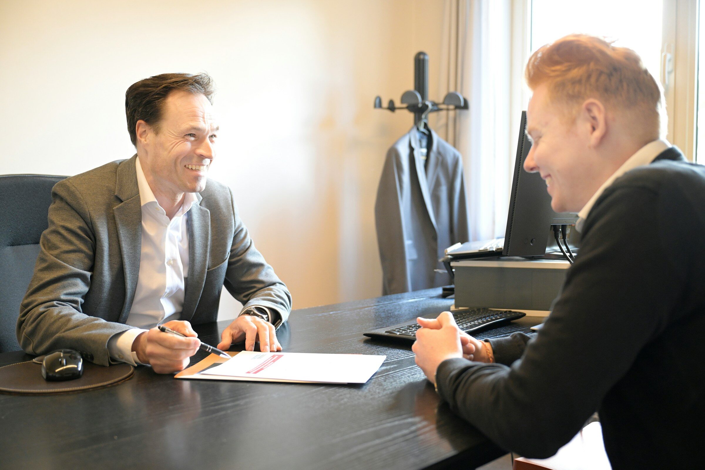 Two men smiling over documents at an office desk
