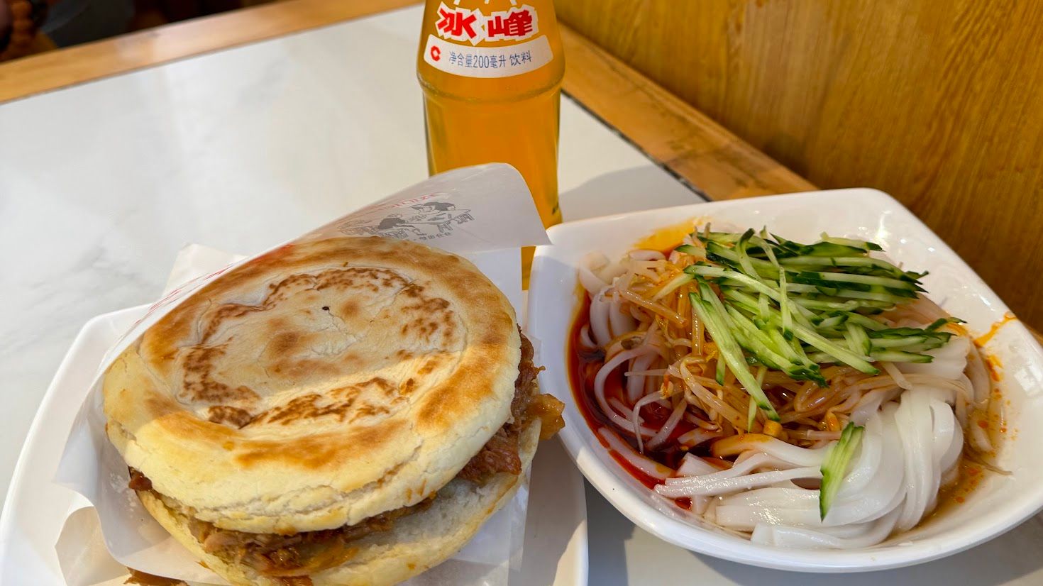 Bread pocket filled with pork and liang pi with cucumber in a dish on a table