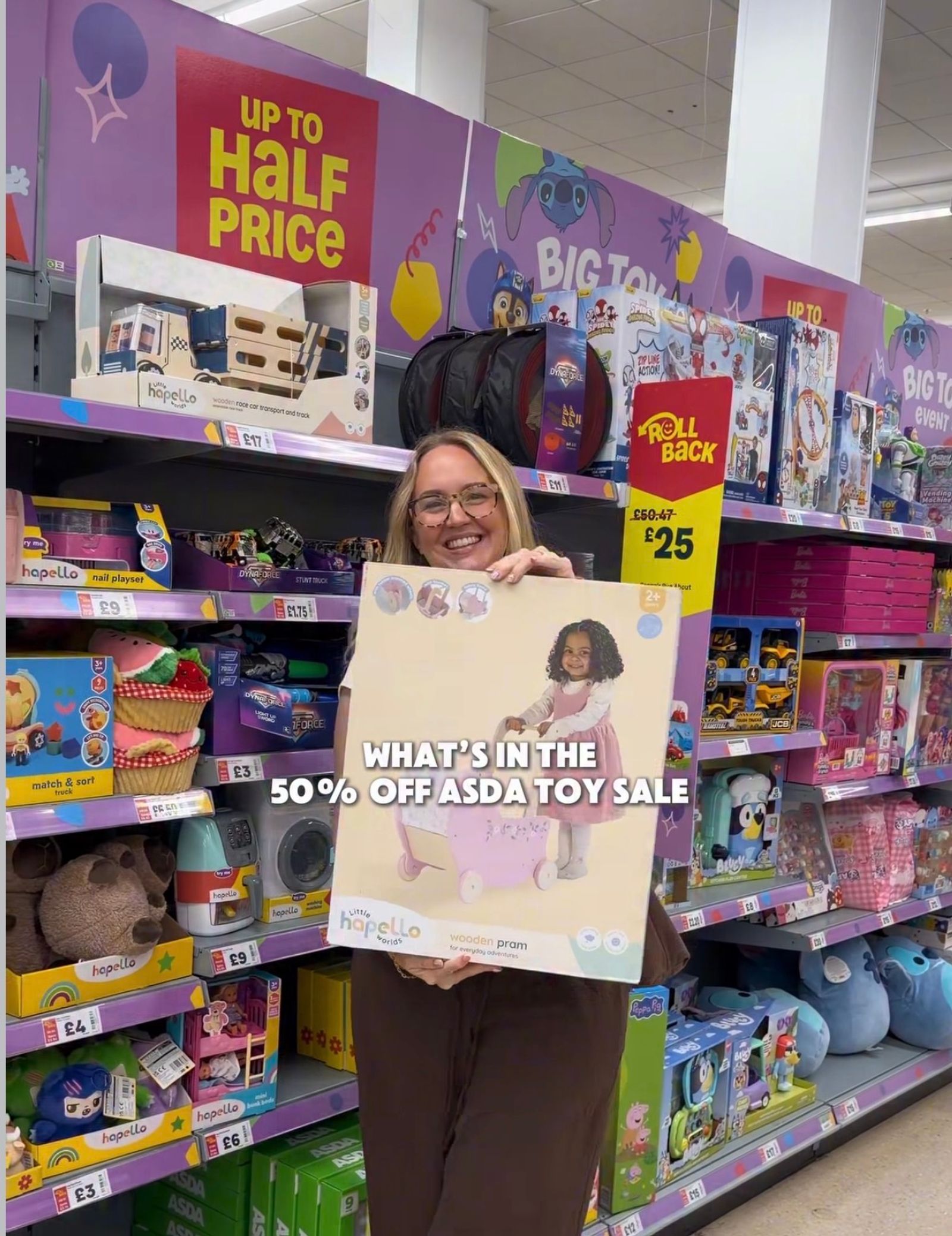 A woman stood in Asda holding lots of toys in an isle full of toys with marked down sale signs on.