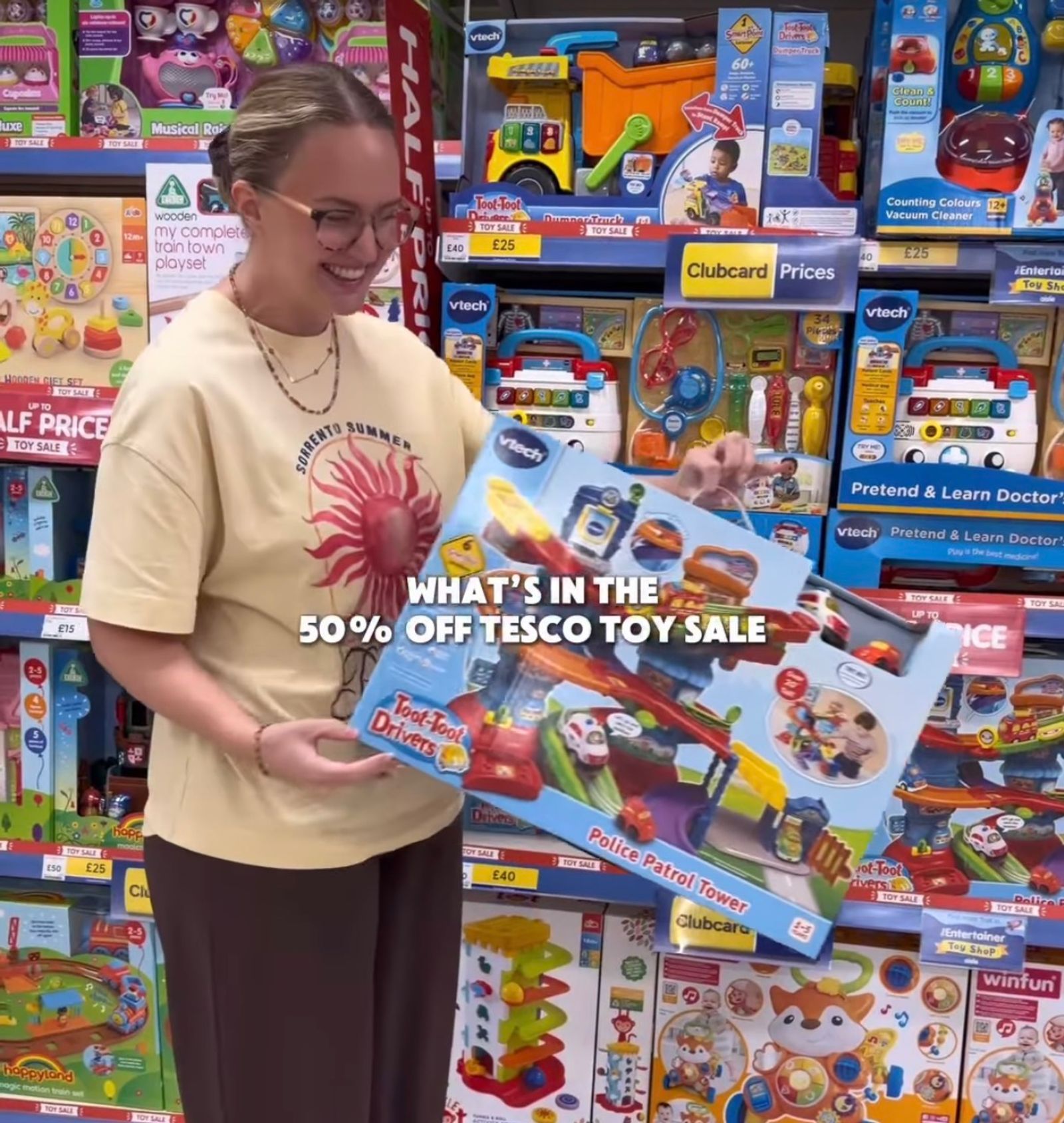 A woman stood in the middle of a shop isle looking at lots of children's toys with big sale signs on.