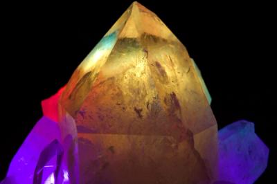 A large, honey-colored quartz crystal is surrounded by smaller crystals in purple, red and blue