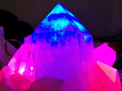 The large quartz crystal is overloaded with blue light, while the supporting crystals turn its base a vibrant purple with their own emissions in red and pink