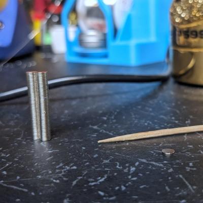 Close-up photo of the tiny (3 x 0.5mm) neodymium magnets used to secure the removable Rhombotron panel next to a toothpick