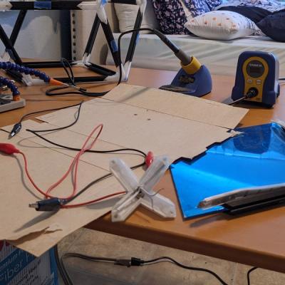 Tabletop with the 4-order vertex with a DC barrel jack installed, an acrylic rhombus, alligator clips, and soldering equipment