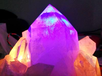 Warm, amber crystals bookend a large central quartz point that glows purple with cyan appearing to emerge from within