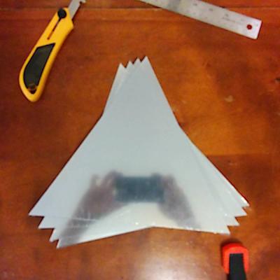 A stack of equilateral triangular half-mirrored acrylic panels surrounded by tools used in the cutting process