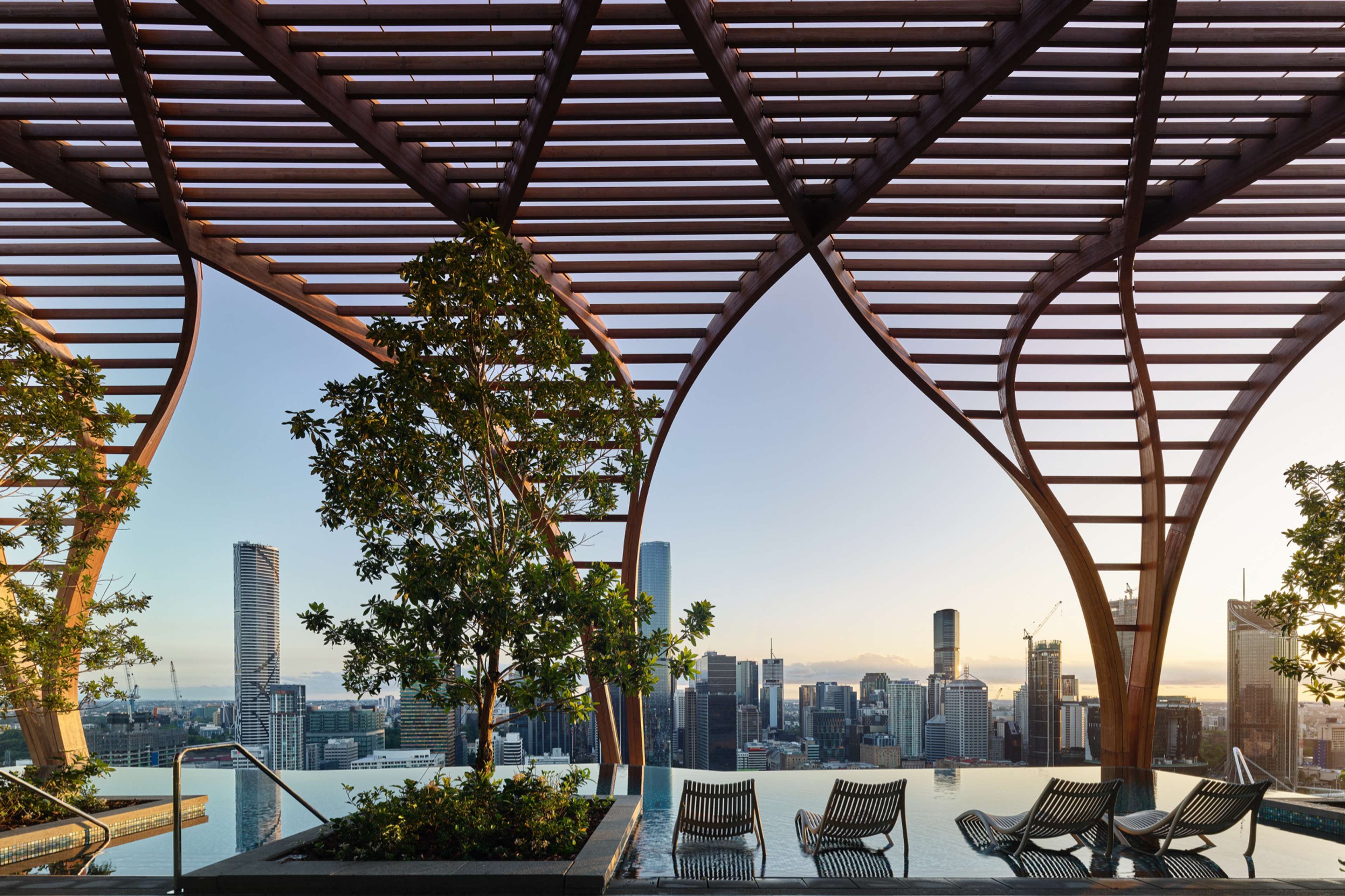 Rooftop infinity pool beneath the timber pergola at Upper House by Aria, looking to the Brisbane skyline