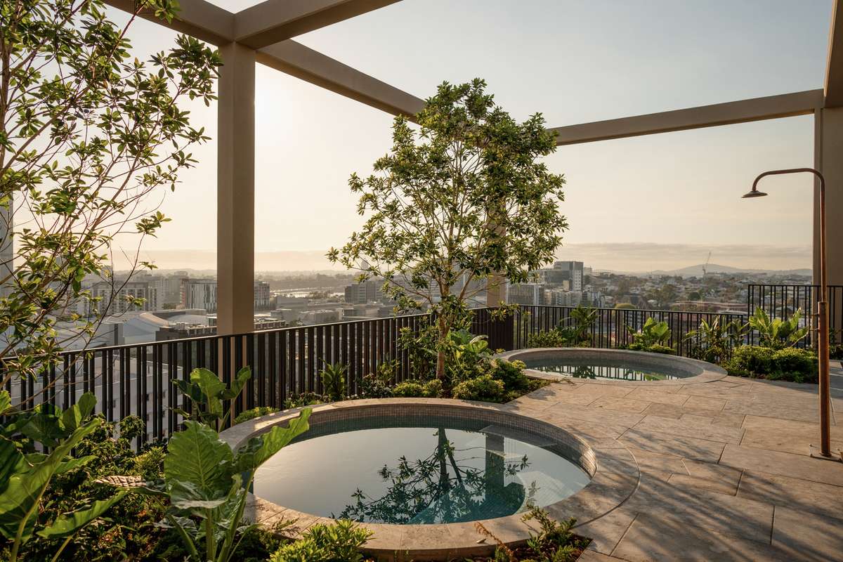 Rooftop pools at Trellis by Aria in Brisbane, surrounded by lush greenery and overlooking the city skyline at sunset.