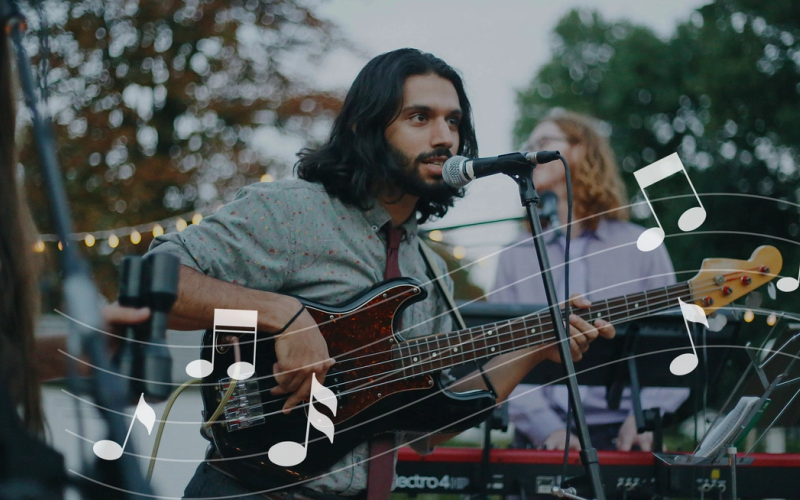 A male artist performing music, in an outdoor setting, surrounded by people appreciating the acoustics.
