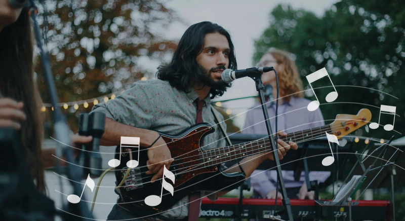 A male artist performing music, in an outdoor setting, surrounded by people appreciating the acoustics.
