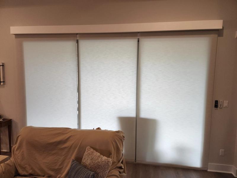 Three white roller shades fully lowered on large sliding glass door in living room