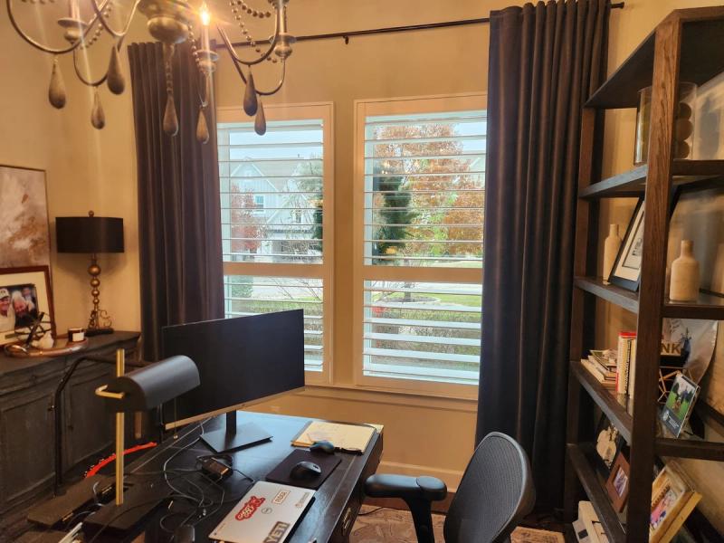 Shutters on double windows in a home office with dark drapery panels