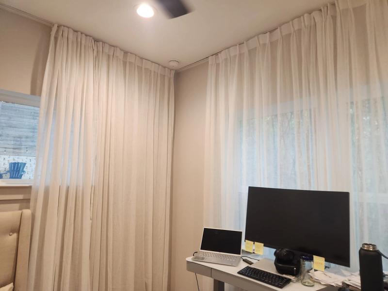 Sheer white pinch-pleat drapery panels on ceiling-mounted track in home office corner