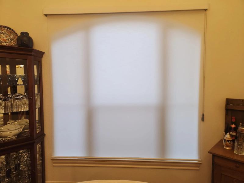 White roller shade fully lowered on large window in dining room with china cabinet
