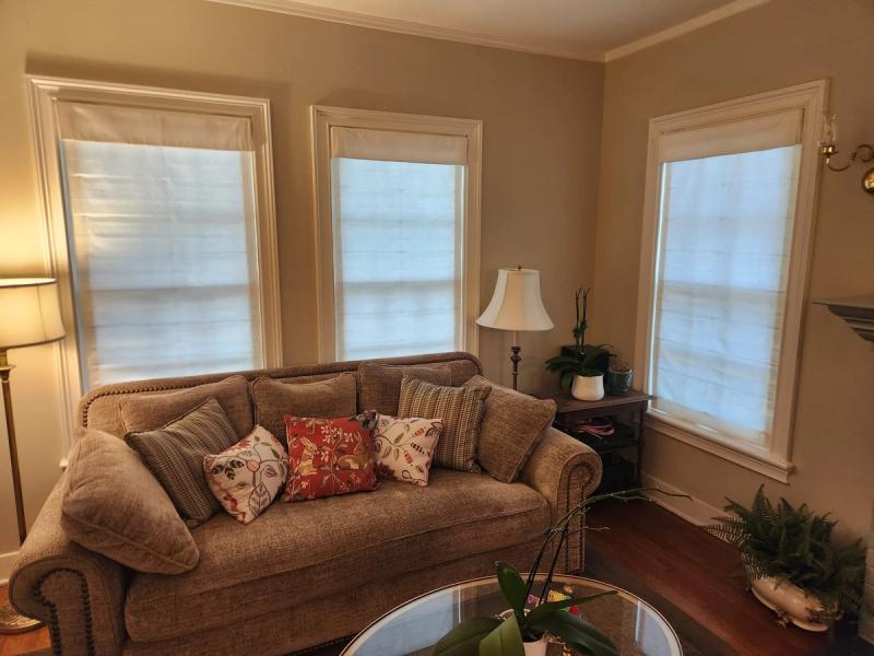 Three white Roman shades on tall windows in a warm-toned living room with sofa