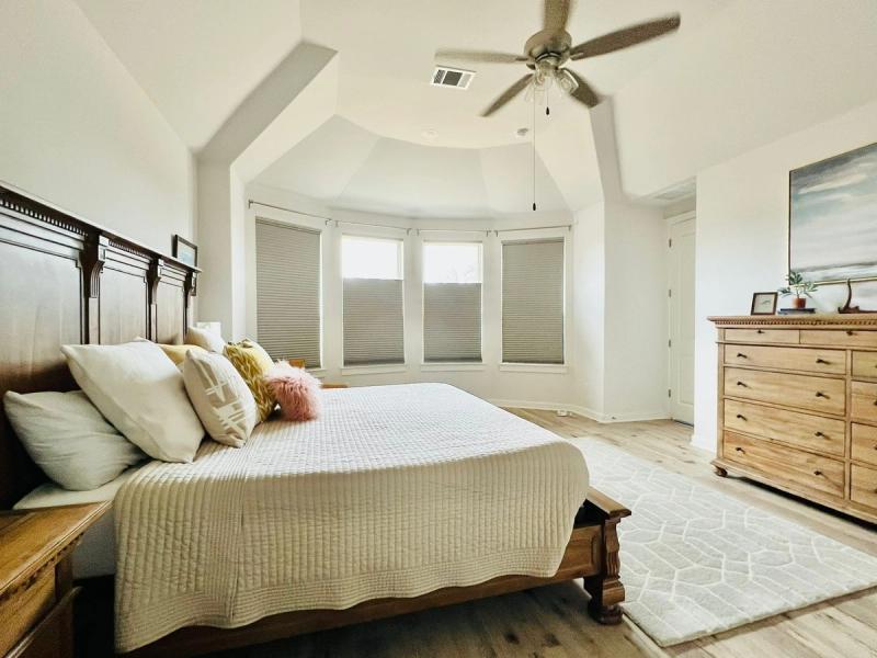 Cellular honeycomb shades on bay windows in a bright master bedroom with wood furniture