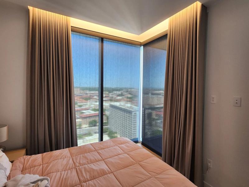 Floor-to-ceiling drapery panels flanking corner windows with solar shades in high-rise bedroom