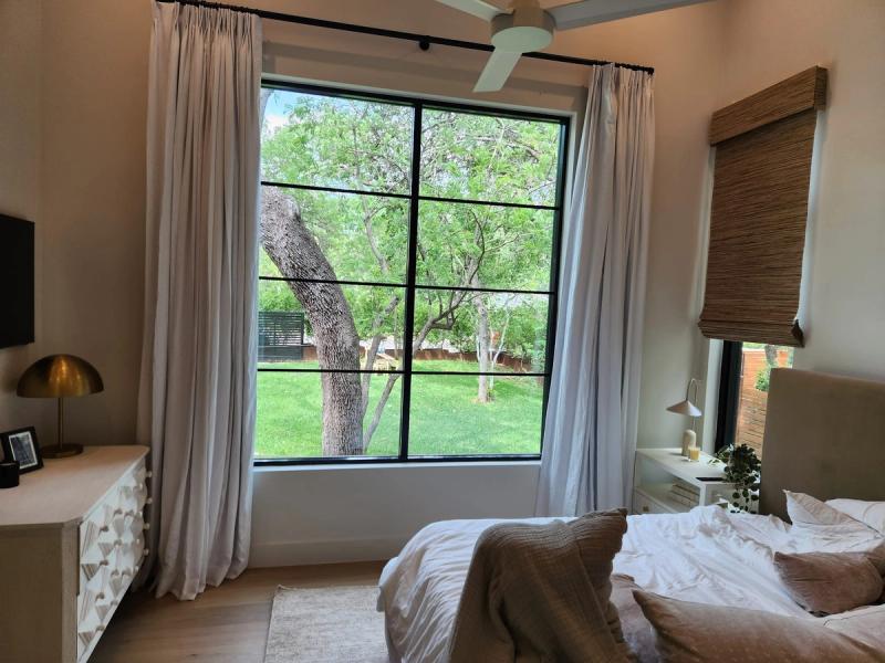 White pinch-pleat drapery panels flanking large black-framed window in modern bedroom