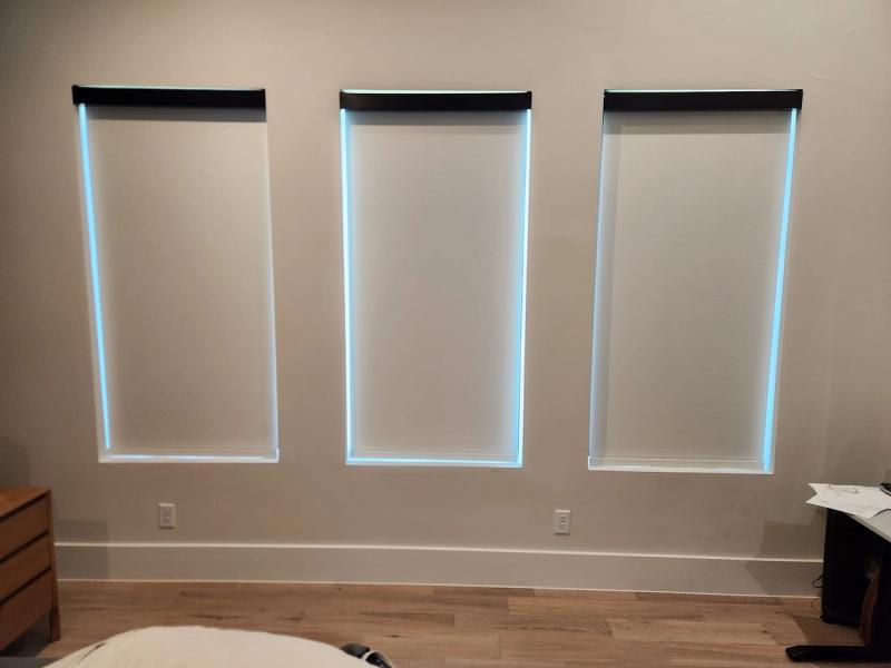Three white roller shades on recessed windows with blue light edge glow, bedroom setting