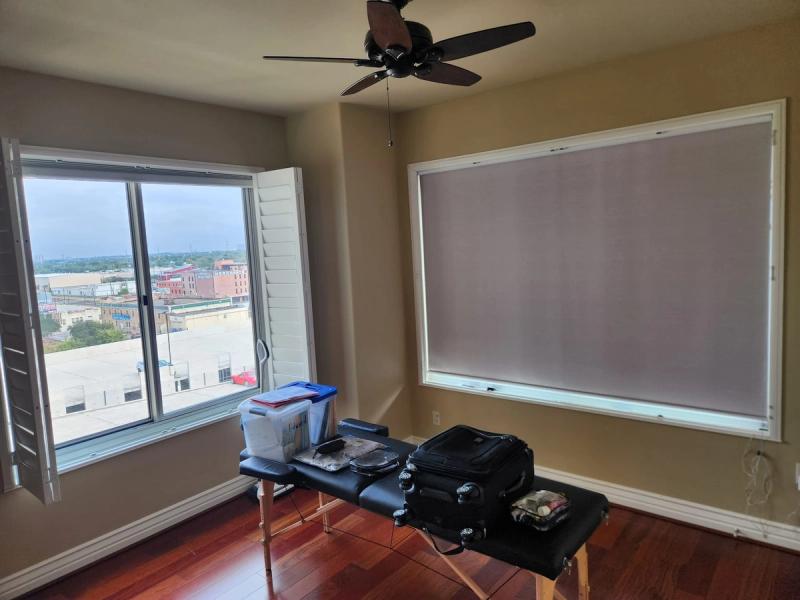 Roller shade on large window in sparse urban high-rise room with massage table