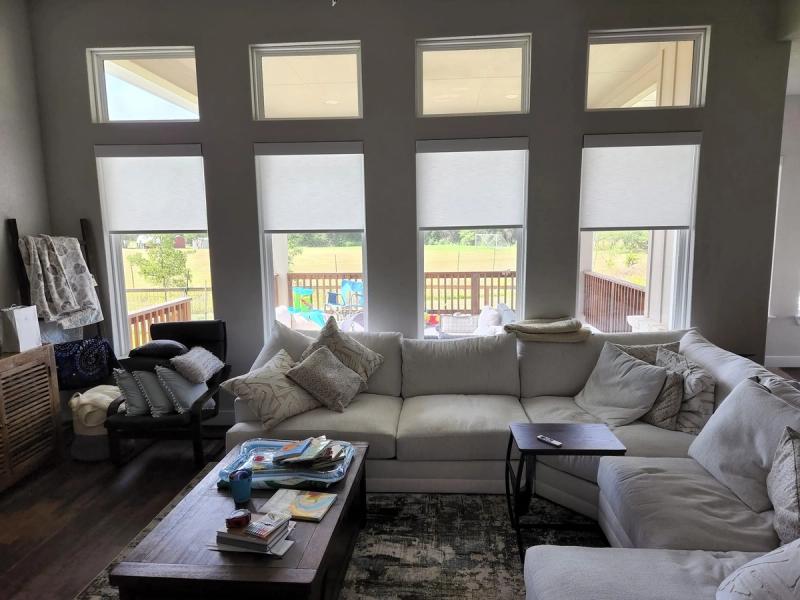 Manual roller solar shades on four tall windows in a bright living room