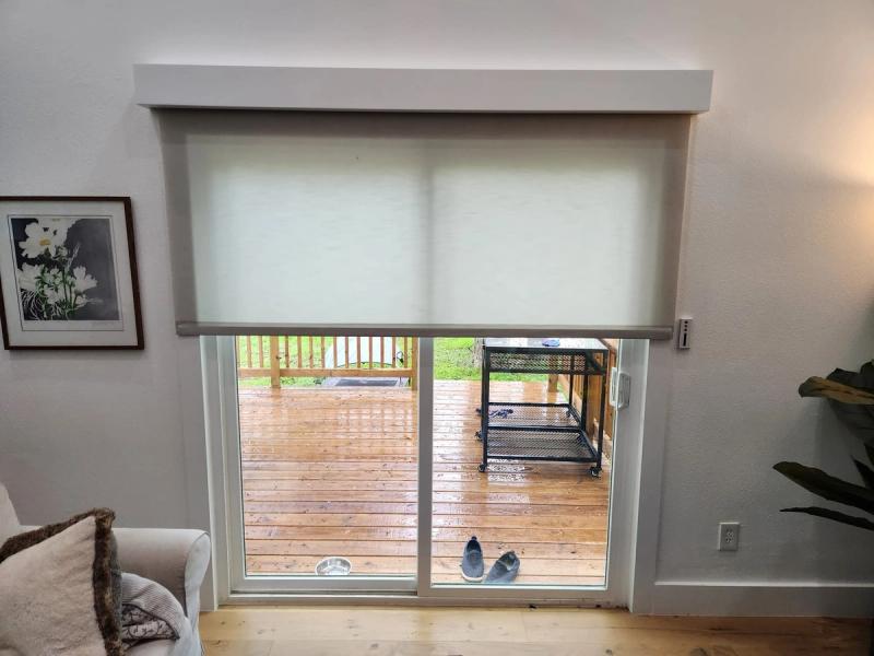 White roller shade partially lowered over sliding glass patio door in bright living room
