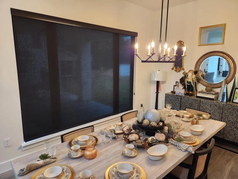 Dark solar roller shades covering large window in elegantly set dining room