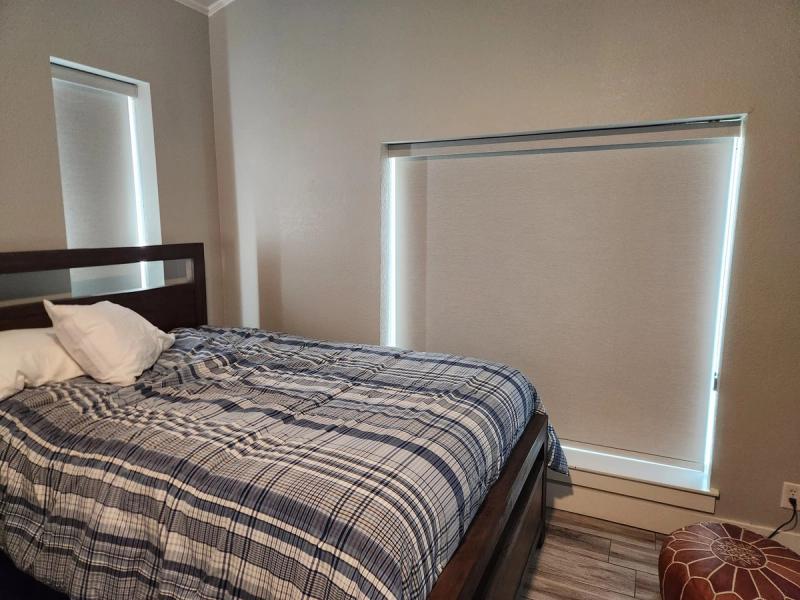 Light-filtering roller shades on bedroom windows with bright light edges, plaid bedding