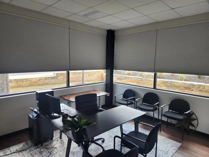 Gray cellular honeycomb shades partially lowered on corner office windows with seating area