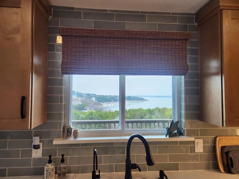 Woven wood Roman shade partially raised over kitchen sink window with lake view