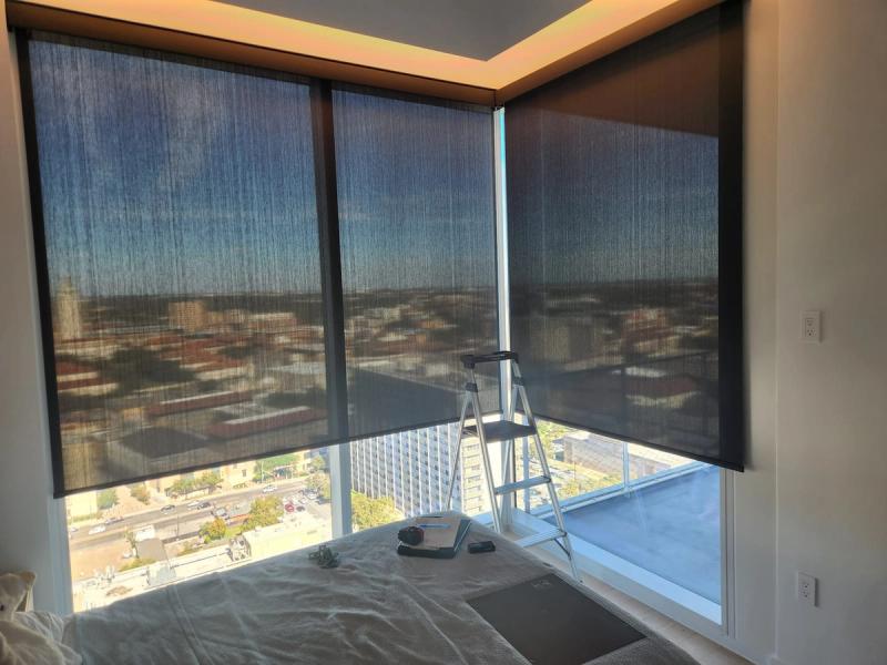 Dark solar roller shades on floor-to-ceiling corner windows in high-rise bedroom