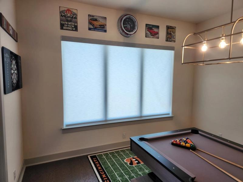 Three white cellular shades covering a wide window in a game room with pool table