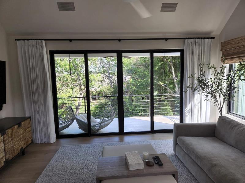 White linen drapery panels on black rod framing large sliding glass doors in modern living room