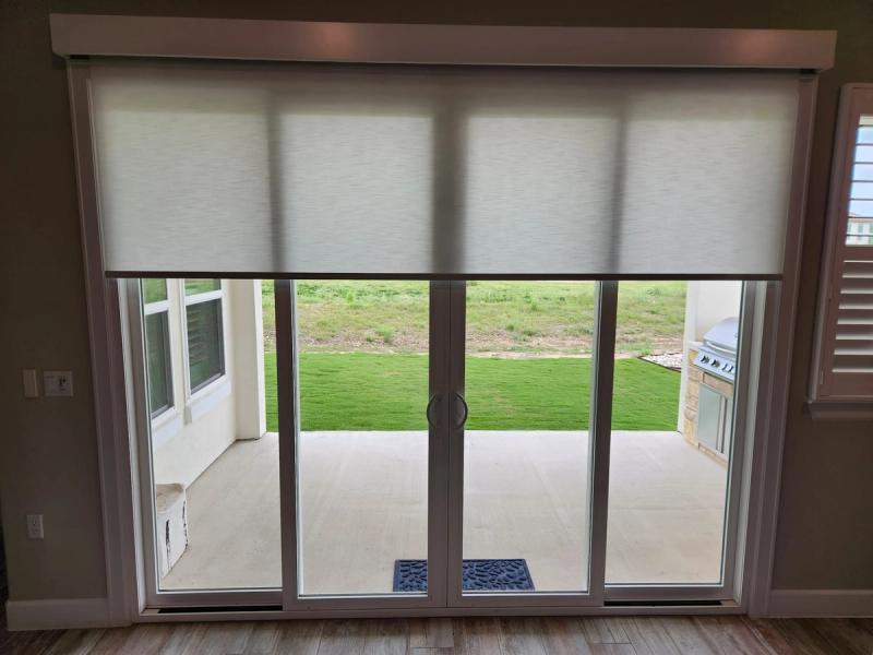 White solar roller shades partially lowered over wide sliding glass patio doors