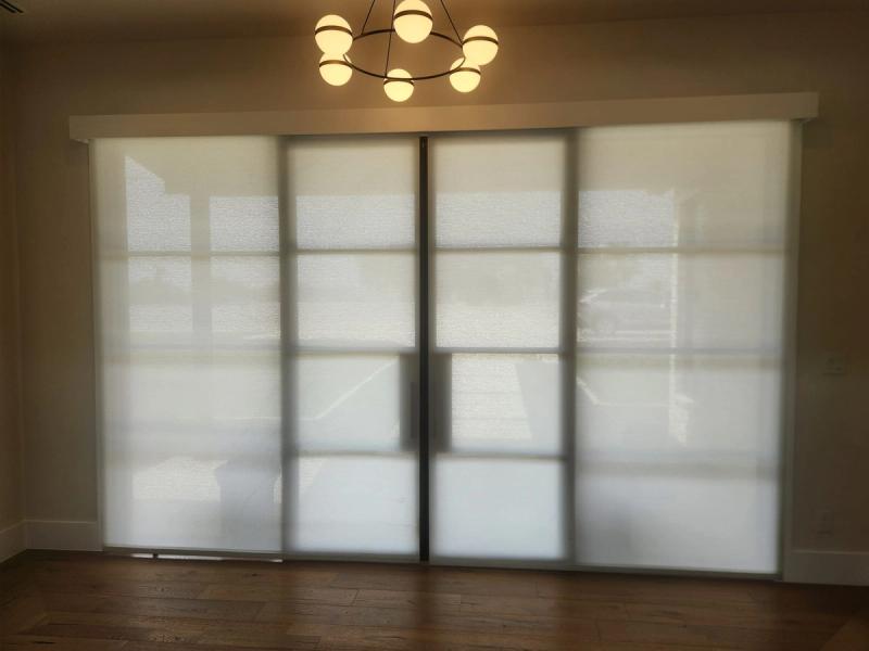 White solar roller shades fully lowered on large sliding glass doors in dining room