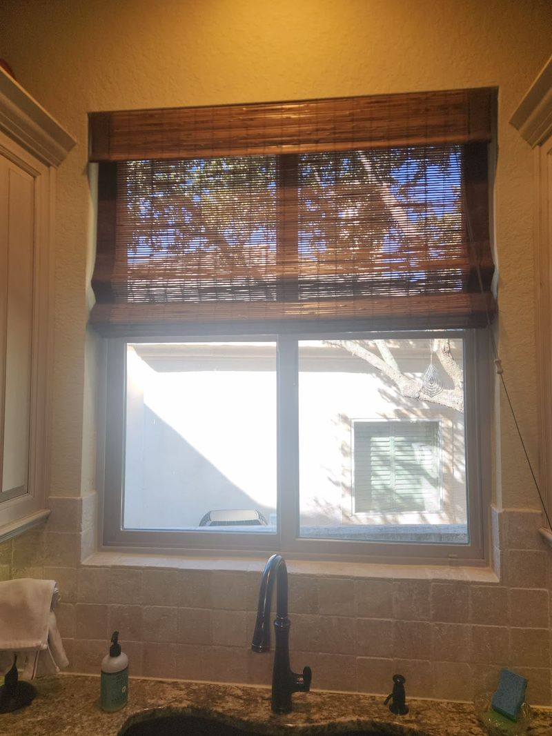 Woven bamboo roman shade partially raised over kitchen sink window