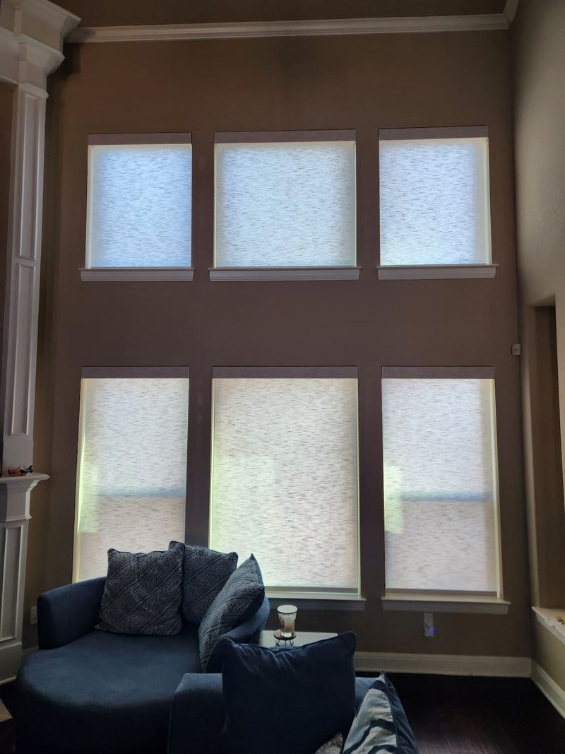 Six roller shades on tall two-story windows in a living room with navy sofa