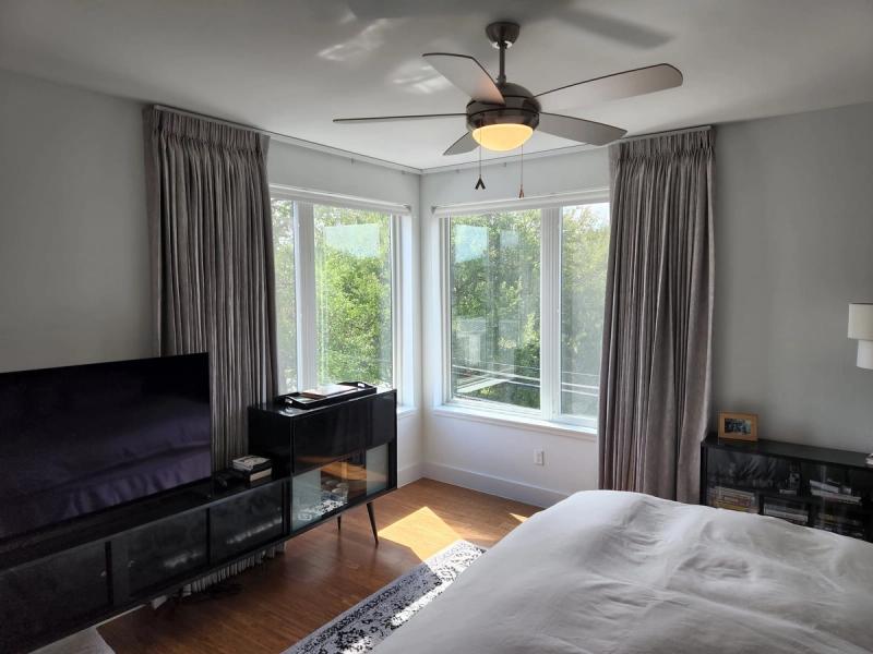 Gray pinch-pleat drapery panels flanking corner windows in a modern bedroom