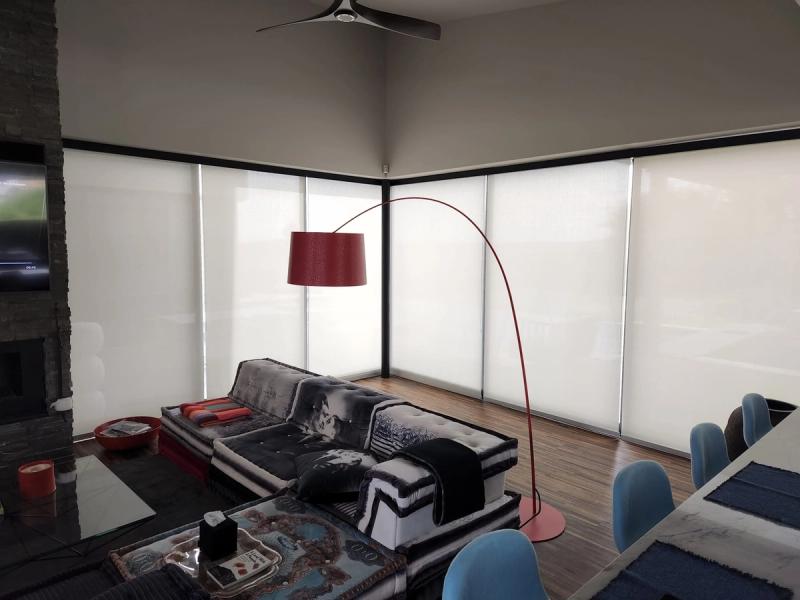 White solar roller shades covering floor-to-ceiling corner windows in modern living room