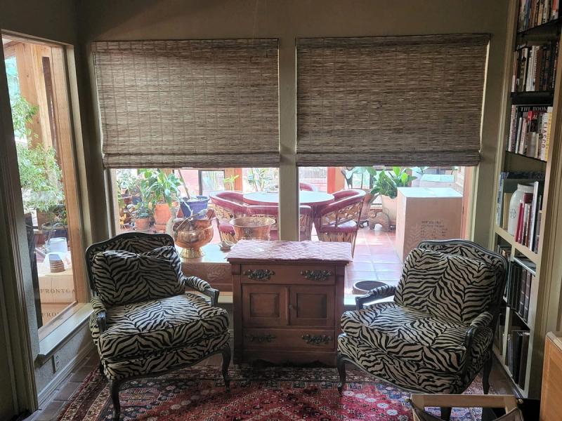 Woven wood Roman shades partially lowered over two large windows in a reading nook with zebra-print chairs