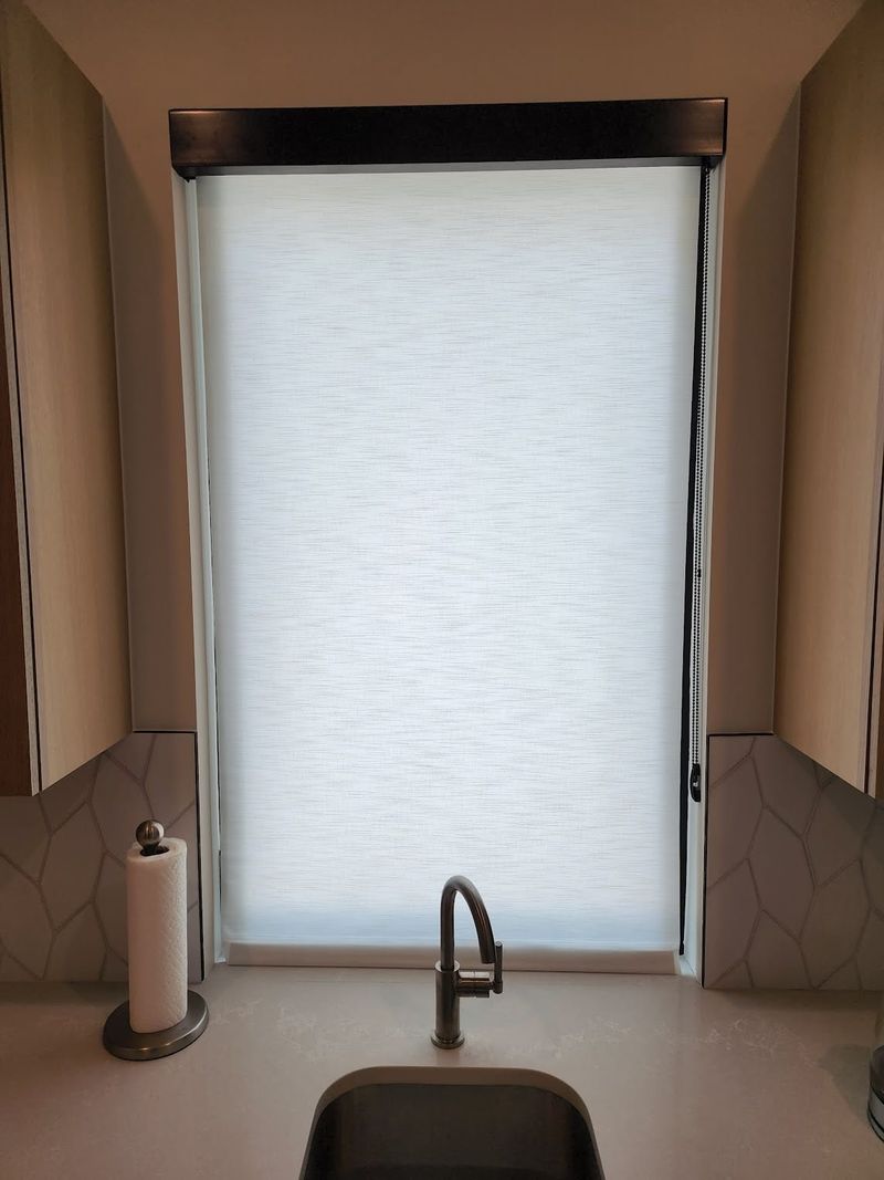White roller shade fully lowered over kitchen sink window with chain control
