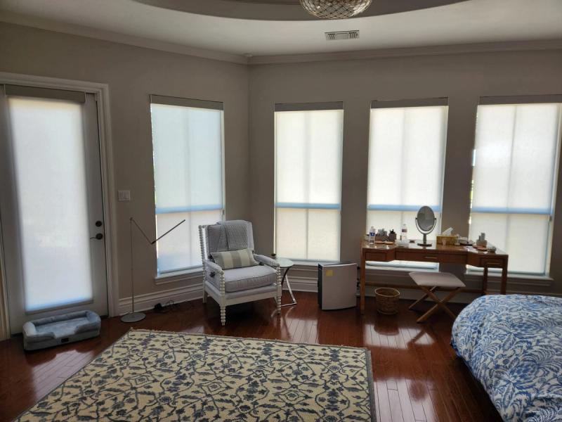 Manual roller solar shades on bay windows in a master bedroom with hardwood floors