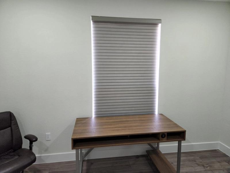 White cellular honeycomb shade fully lowered over window above wooden desk