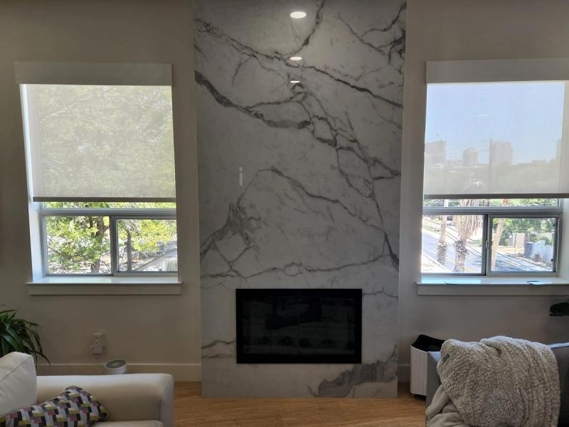 Solar roller shades on two living room windows flanking a marble fireplace