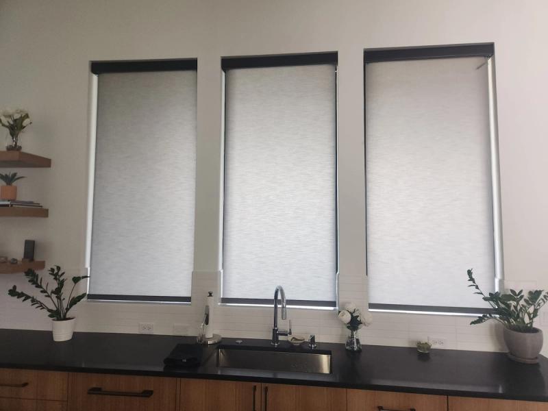 Three white roller shades fully lowered over kitchen sink windows, black countertop