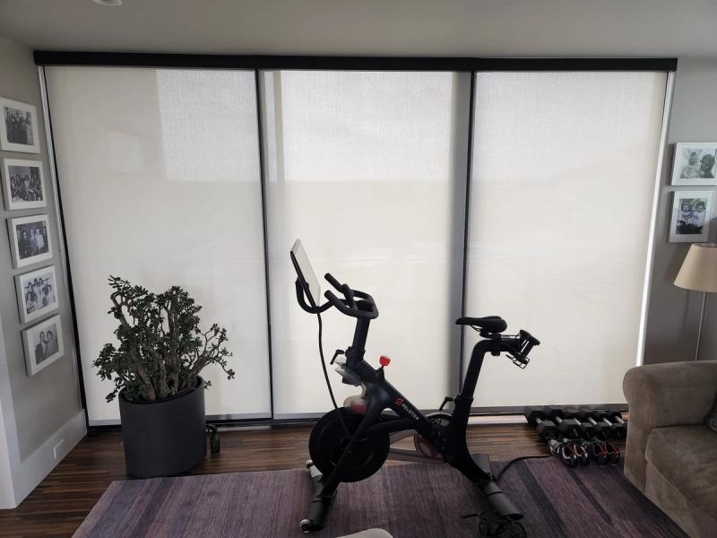 Three white solar roller shades covering large sliding glass doors in home gym